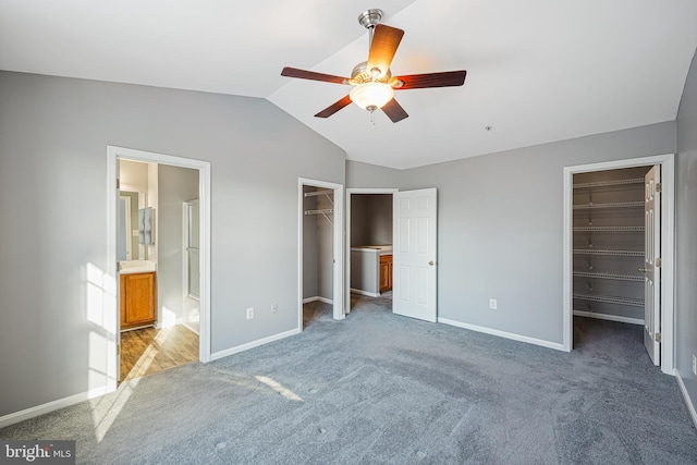 unfurnished bedroom featuring ceiling fan, a spacious closet, ensuite bathroom, light colored carpet, and lofted ceiling