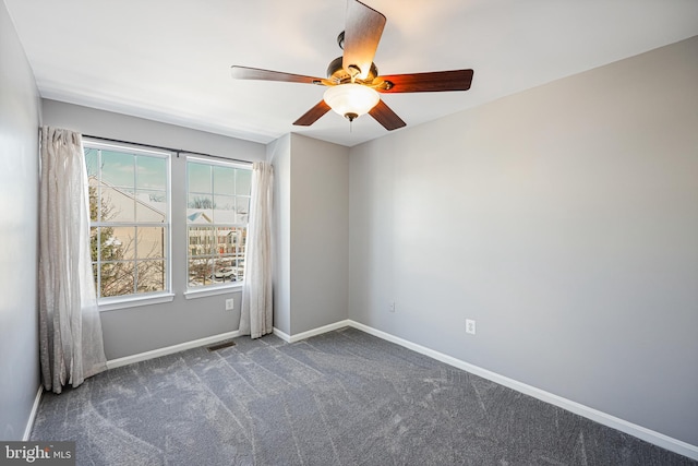 spare room with a wealth of natural light, ceiling fan, and dark colored carpet