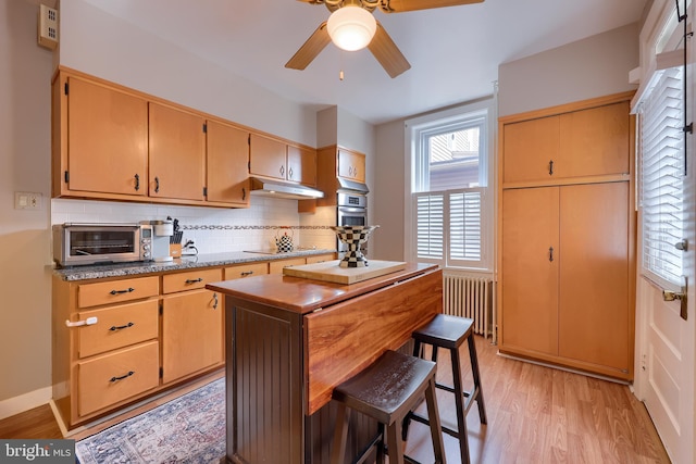 kitchen featuring light wood-type flooring, tasteful backsplash, radiator, black electric cooktop, and ceiling fan