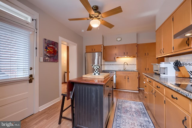 kitchen featuring appliances with stainless steel finishes, backsplash, a kitchen breakfast bar, sink, and light hardwood / wood-style floors