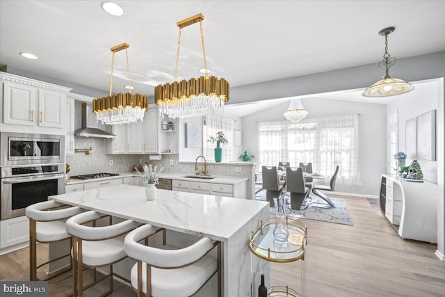 kitchen with white cabinetry, wall chimney range hood, tasteful backsplash, a kitchen bar, and appliances with stainless steel finishes