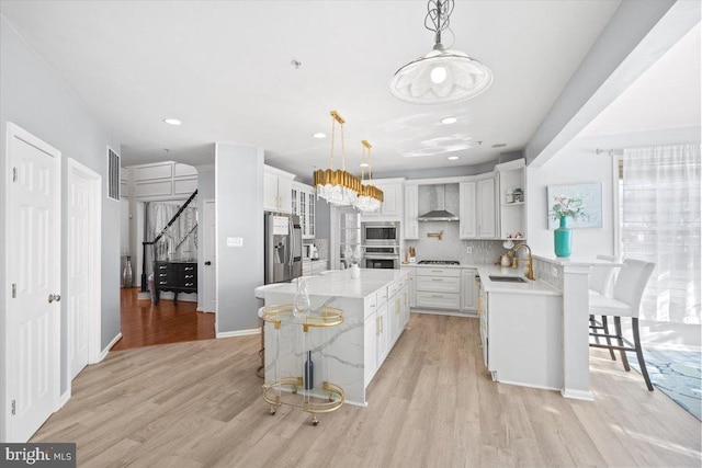 kitchen featuring hanging light fixtures, light hardwood / wood-style flooring, wall chimney exhaust hood, a breakfast bar area, and stainless steel appliances