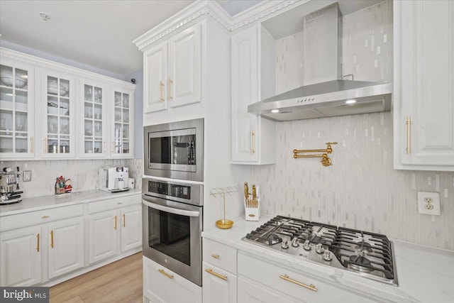 kitchen featuring light wood-type flooring, stainless steel appliances, white cabinetry, and wall chimney range hood