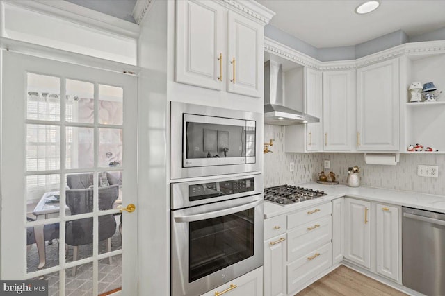 kitchen with white cabinets, appliances with stainless steel finishes, light wood-type flooring, and wall chimney range hood