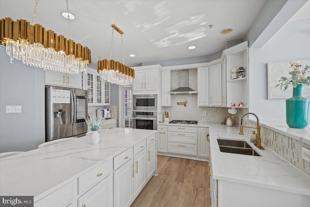 kitchen with sink, wall chimney exhaust hood, stainless steel appliances, pendant lighting, and white cabinets