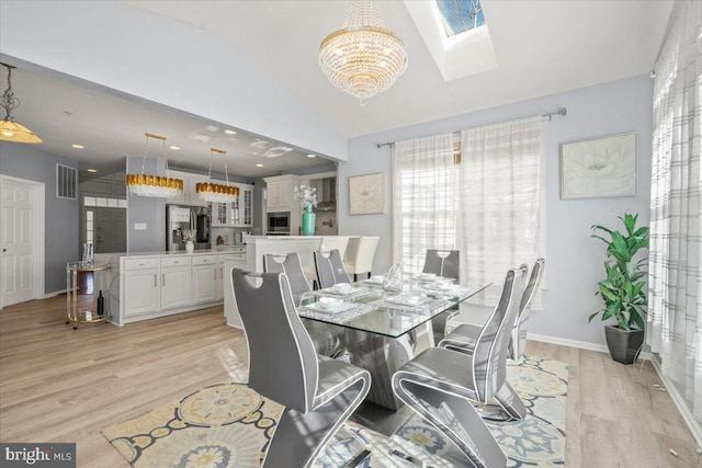 dining space featuring light hardwood / wood-style floors, an inviting chandelier, and vaulted ceiling with skylight