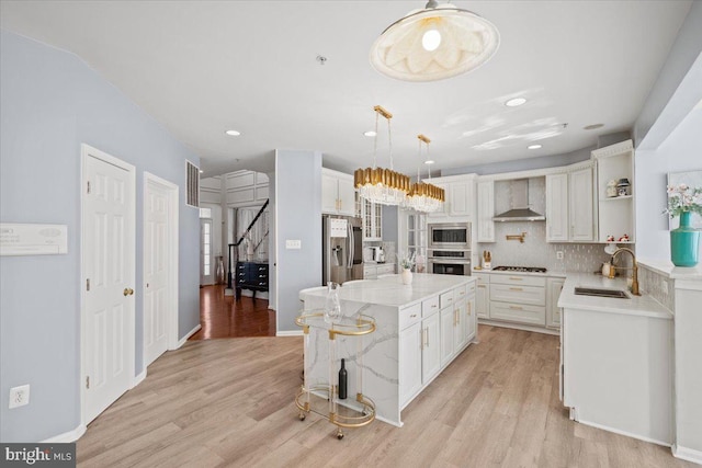 kitchen with appliances with stainless steel finishes, wall chimney range hood, sink, light hardwood / wood-style flooring, and a kitchen island