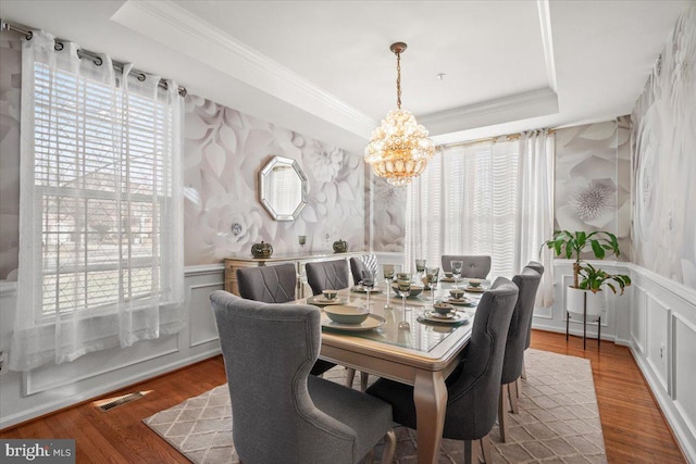 dining space featuring a raised ceiling, wood-type flooring, ornamental molding, and a chandelier