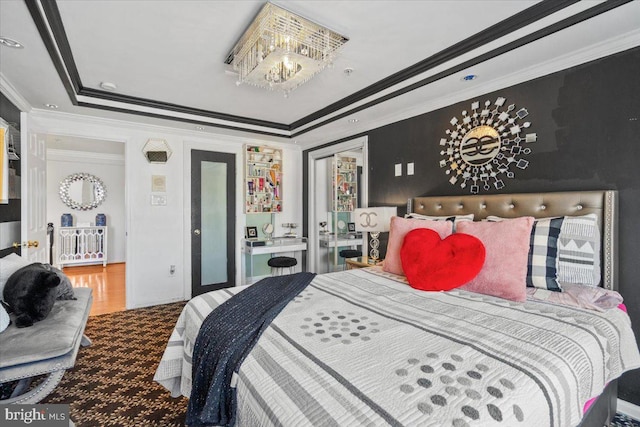 bedroom with a tray ceiling, crown molding, hardwood / wood-style floors, and a notable chandelier