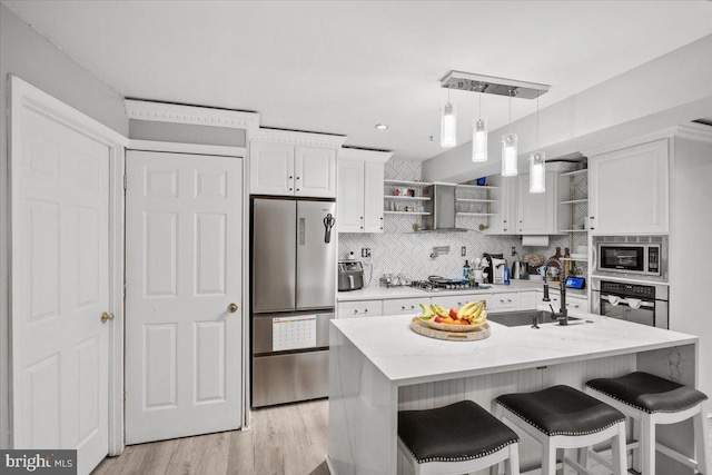 kitchen with a kitchen island with sink, light wood-type flooring, appliances with stainless steel finishes, light stone counters, and white cabinetry