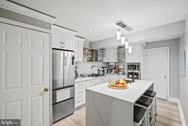 kitchen with light stone countertops, an island with sink, decorative light fixtures, white cabinets, and appliances with stainless steel finishes