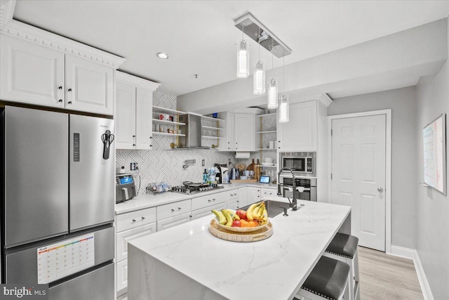 kitchen featuring a center island with sink, light stone countertops, appliances with stainless steel finishes, white cabinetry, and a breakfast bar area