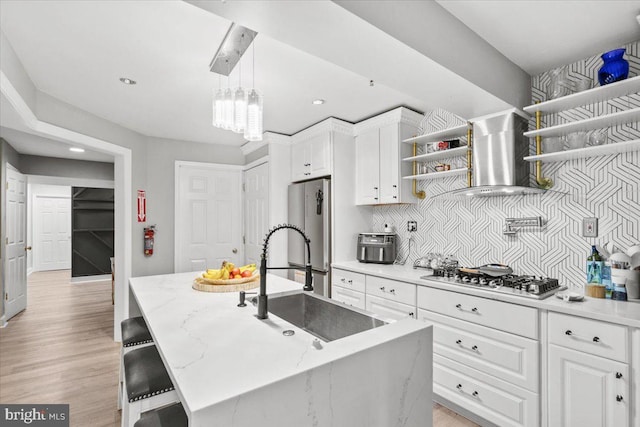 kitchen featuring a center island with sink, stainless steel appliances, wall chimney range hood, and light wood-type flooring