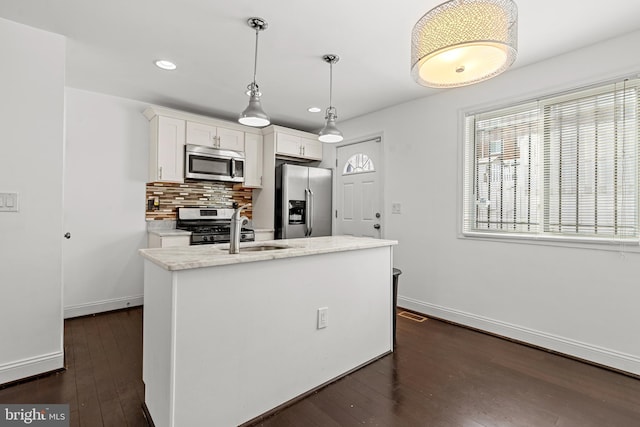 kitchen with appliances with stainless steel finishes, backsplash, a kitchen island with sink, white cabinets, and hanging light fixtures