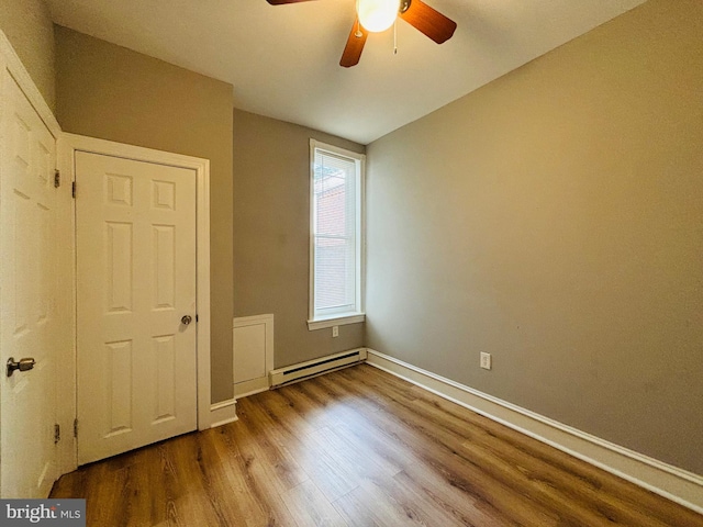 unfurnished bedroom with hardwood / wood-style floors, a closet, ceiling fan, and a baseboard heating unit