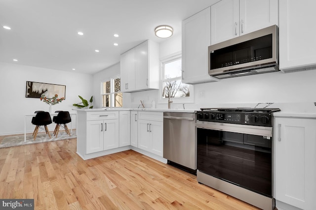 kitchen with white cabinets, stainless steel appliances, and light hardwood / wood-style flooring