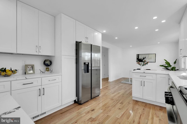 kitchen with appliances with stainless steel finishes, light wood-type flooring, white cabinetry, and light stone counters