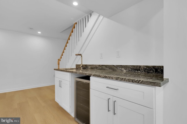 kitchen featuring dark stone counters, white cabinets, sink, light wood-type flooring, and beverage cooler