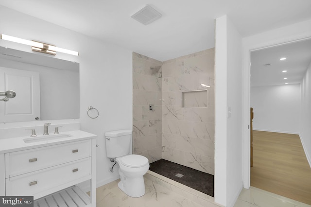 bathroom with a tile shower, vanity, toilet, and hardwood / wood-style floors