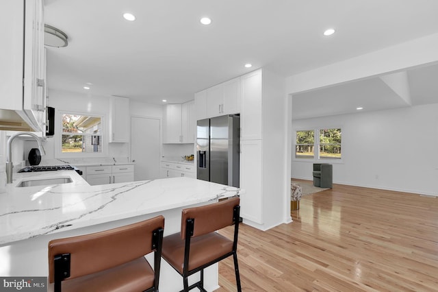 kitchen featuring kitchen peninsula, stainless steel refrigerator with ice dispenser, sink, light hardwood / wood-style floors, and white cabinetry