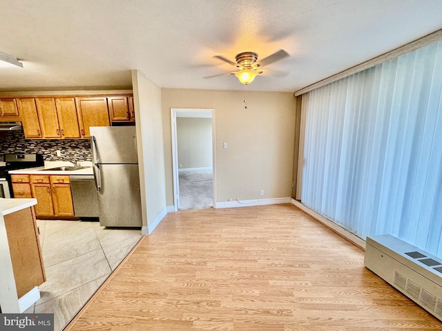 kitchen with decorative backsplash, light wood-type flooring, stainless steel appliances, ceiling fan, and sink