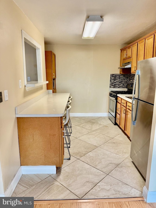 kitchen with decorative backsplash, appliances with stainless steel finishes, a kitchen bar, and a textured ceiling