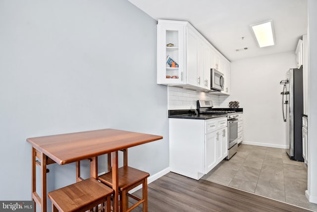 kitchen with decorative backsplash, white cabinetry, wood-type flooring, and appliances with stainless steel finishes