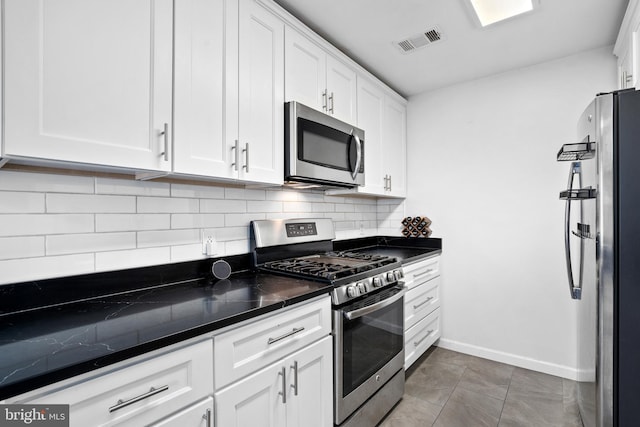 kitchen featuring decorative backsplash, white cabinets, dark tile patterned flooring, and appliances with stainless steel finishes