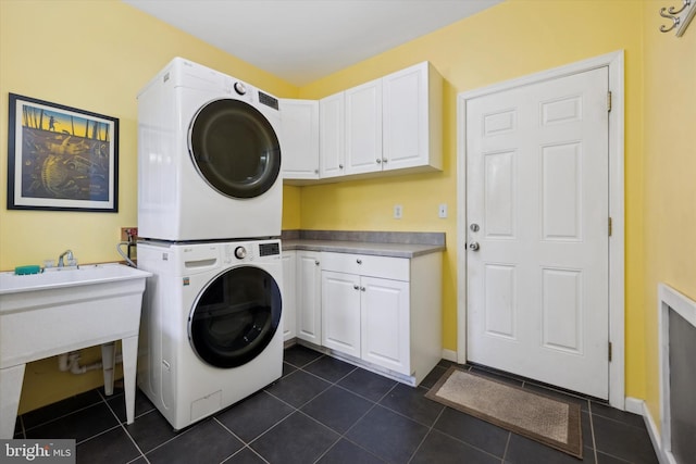 laundry area with cabinets, stacked washing maching and dryer, and dark tile patterned floors