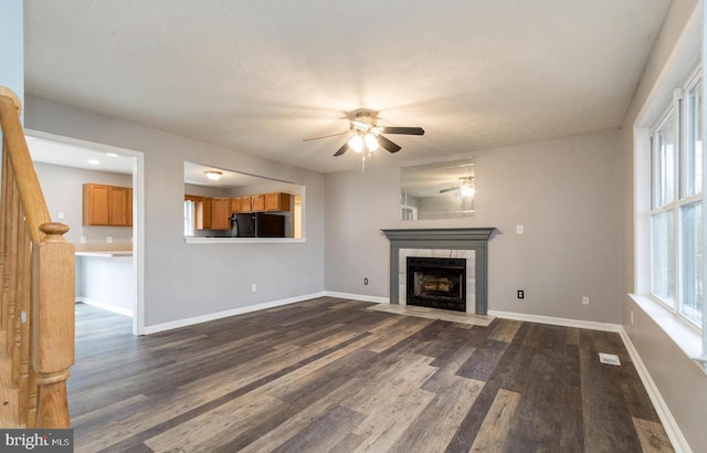 unfurnished living room featuring dark hardwood / wood-style flooring, ceiling fan, and a tiled fireplace