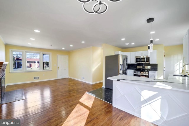 kitchen featuring appliances with stainless steel finishes, tasteful backsplash, dark wood-type flooring, decorative light fixtures, and white cabinetry