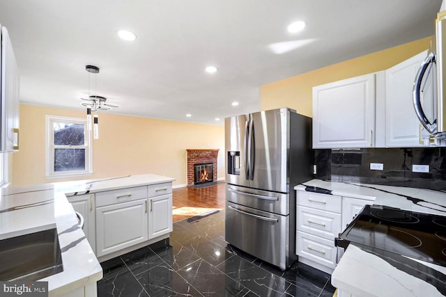 kitchen with white cabinets, appliances with stainless steel finishes, decorative backsplash, and a brick fireplace