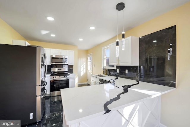 kitchen featuring kitchen peninsula, pendant lighting, decorative backsplash, white cabinets, and appliances with stainless steel finishes