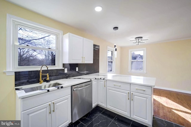 kitchen featuring kitchen peninsula, stainless steel dishwasher, sink, pendant lighting, and white cabinets