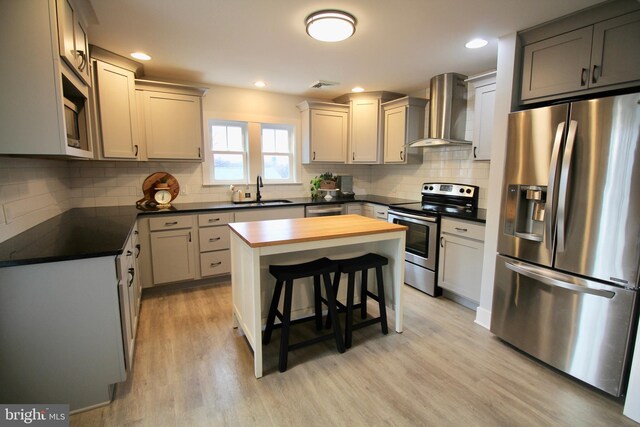 kitchen featuring sink, wall chimney exhaust hood, stainless steel appliances, wood counters, and light hardwood / wood-style flooring