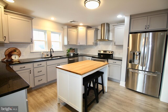 kitchen with sink, wall chimney exhaust hood, wood counters, appliances with stainless steel finishes, and light wood-type flooring