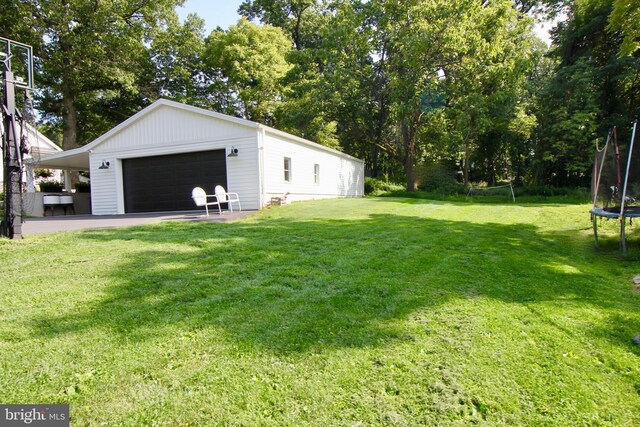 view of yard featuring a garage, a trampoline, and an outbuilding