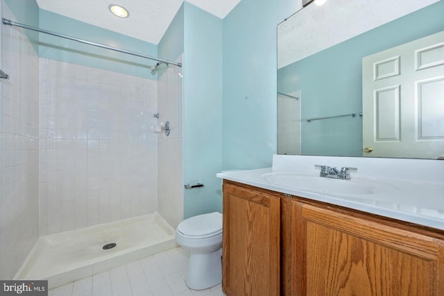 bathroom with a textured ceiling, vanity, tiled shower, tile patterned flooring, and toilet