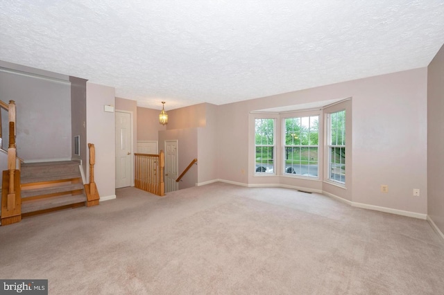 empty room featuring light carpet, a textured ceiling, and an inviting chandelier