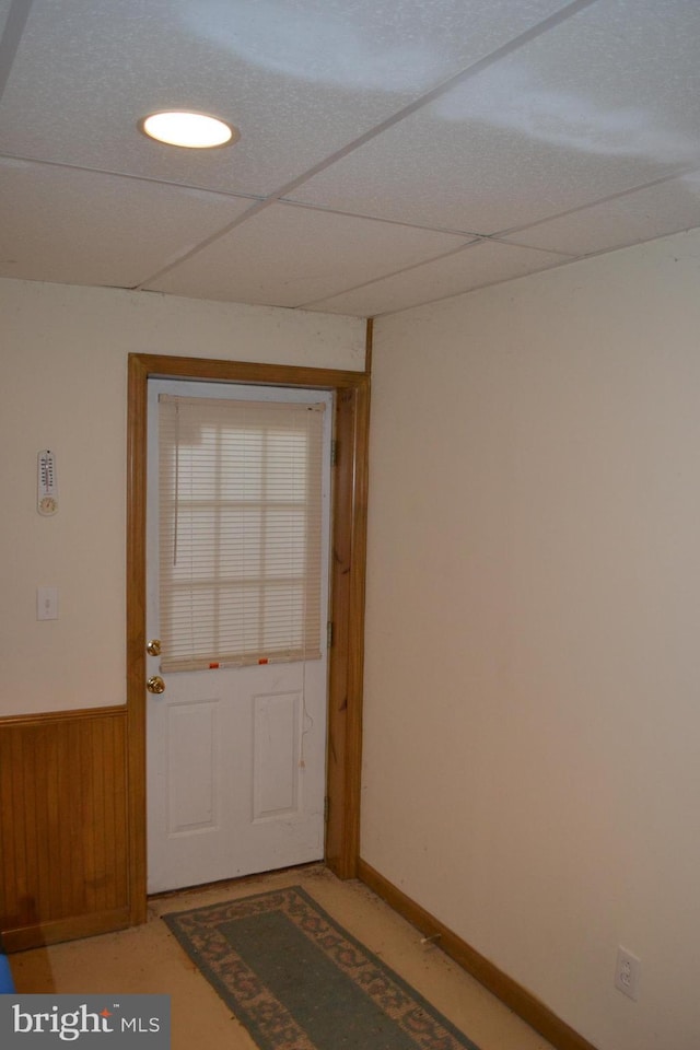 doorway featuring a paneled ceiling and wooden walls