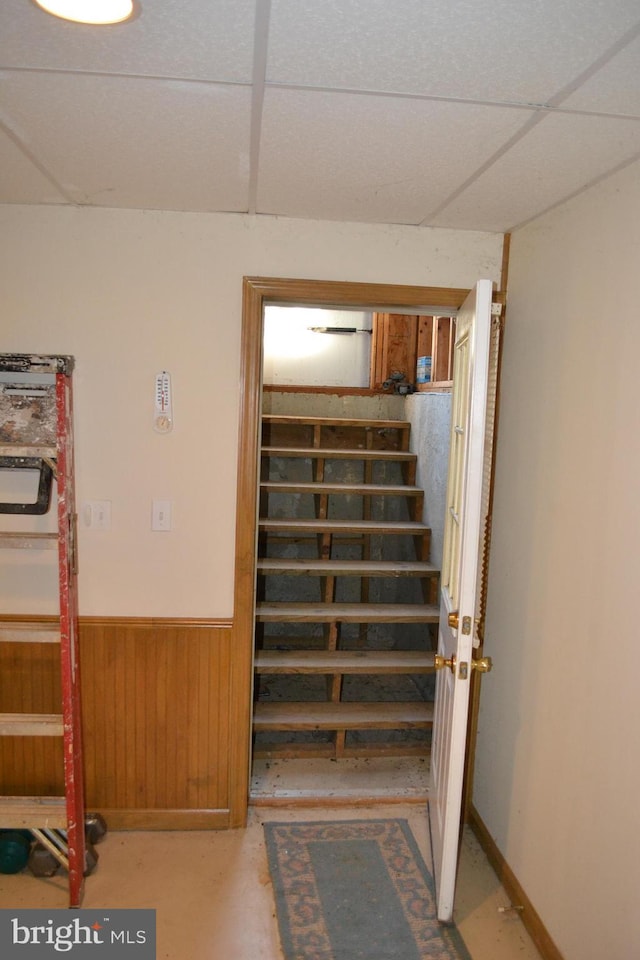 staircase featuring wood walls and a drop ceiling