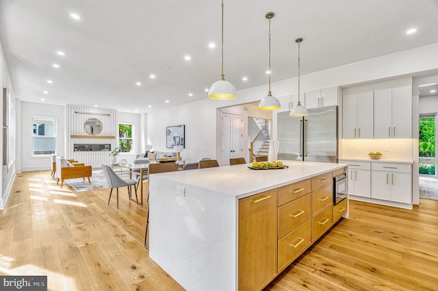 kitchen with white cabinets, light hardwood / wood-style floors, decorative light fixtures, and appliances with stainless steel finishes