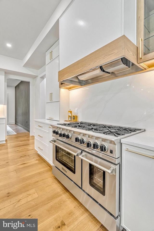 kitchen featuring decorative backsplash, light hardwood / wood-style floors, double oven range, and white cabinetry