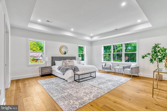 bedroom with a tray ceiling, multiple windows, and light hardwood / wood-style flooring