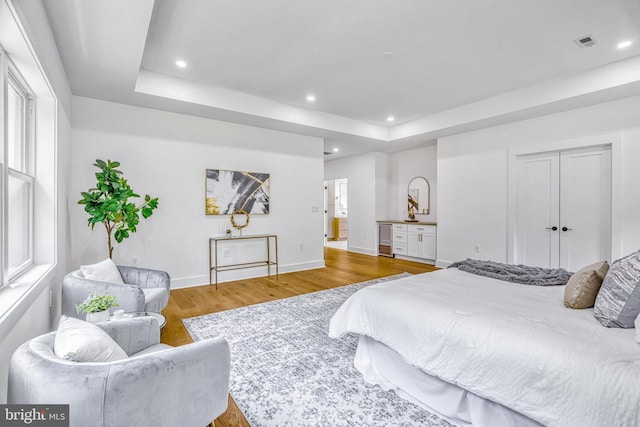 bedroom featuring a raised ceiling, wood-type flooring, and wine cooler