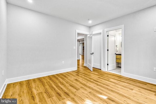 unfurnished bedroom with ensuite bathroom and light wood-type flooring