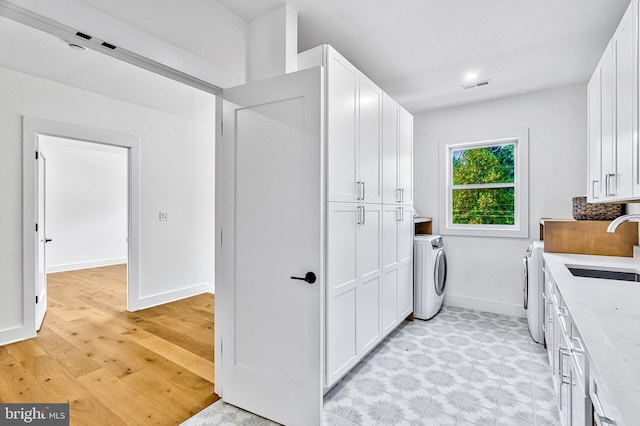 laundry area featuring washing machine and clothes dryer, light hardwood / wood-style flooring, and sink