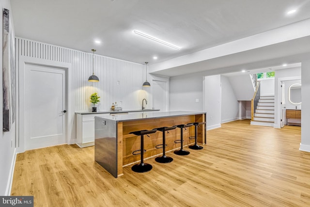 bar featuring white cabinets, light hardwood / wood-style flooring, hanging light fixtures, and sink