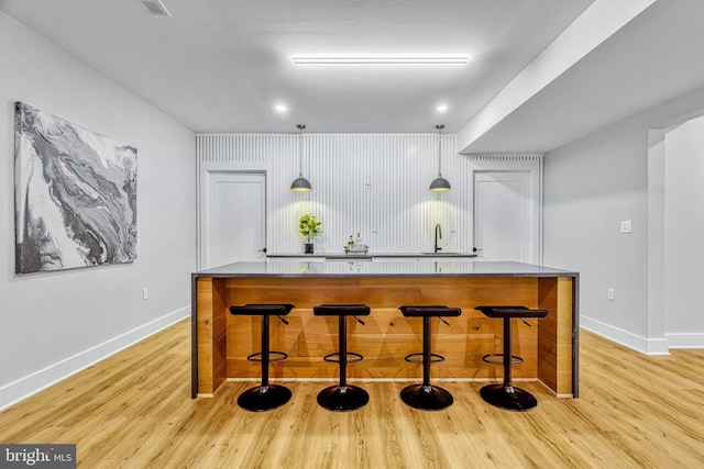 bar featuring decorative light fixtures, sink, and light hardwood / wood-style flooring