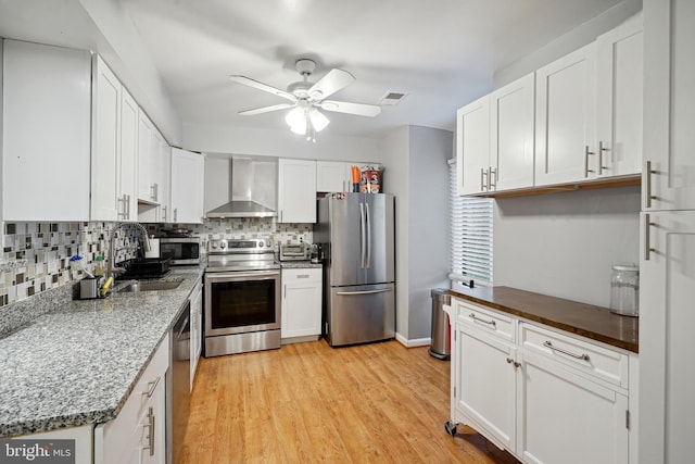 kitchen featuring white cabinets, stainless steel appliances, and wall chimney range hood